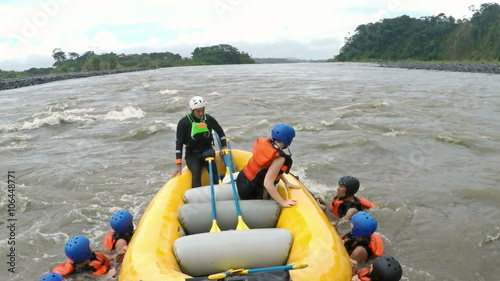 A group of rafters in a yellow raft assists teammates who have fallen into the rushing river near Banos, Ecuador, helping them back aboard amid choppy water, a small waterfall behind.