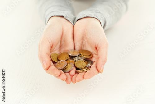 Young woman in grey shirt holding a heap of euro coins in her hands above white wooden surface, close up