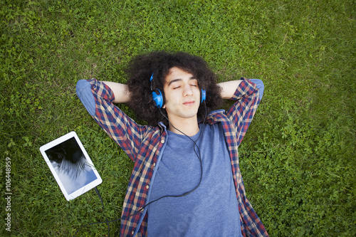 Young man lying on grass and listening music photo