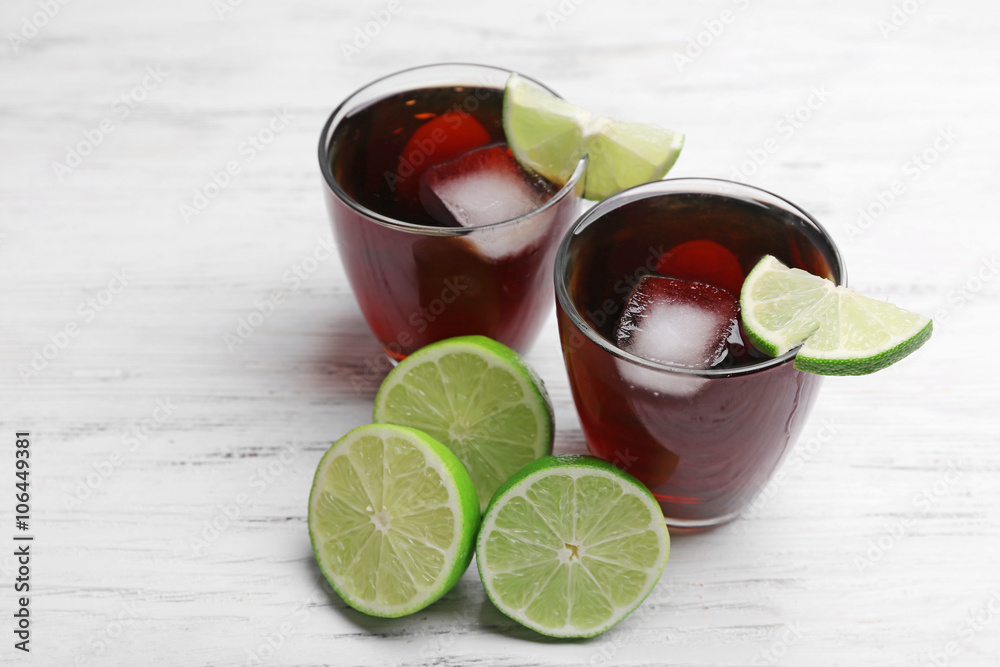 Two glasses of cola with ice, mint and lime on white wooden table background Two glasses of cola with ice, mint and lime on white wooden table background