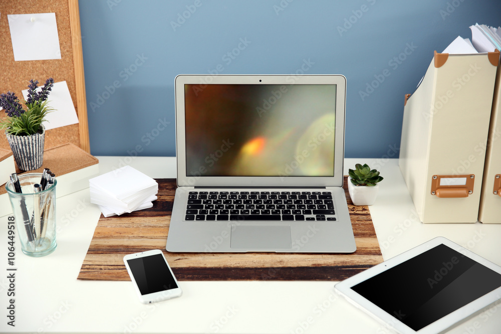 Workplace with different devices, stationery and table on blue wall background Workplace with different devices, stationery and table on blue wall background