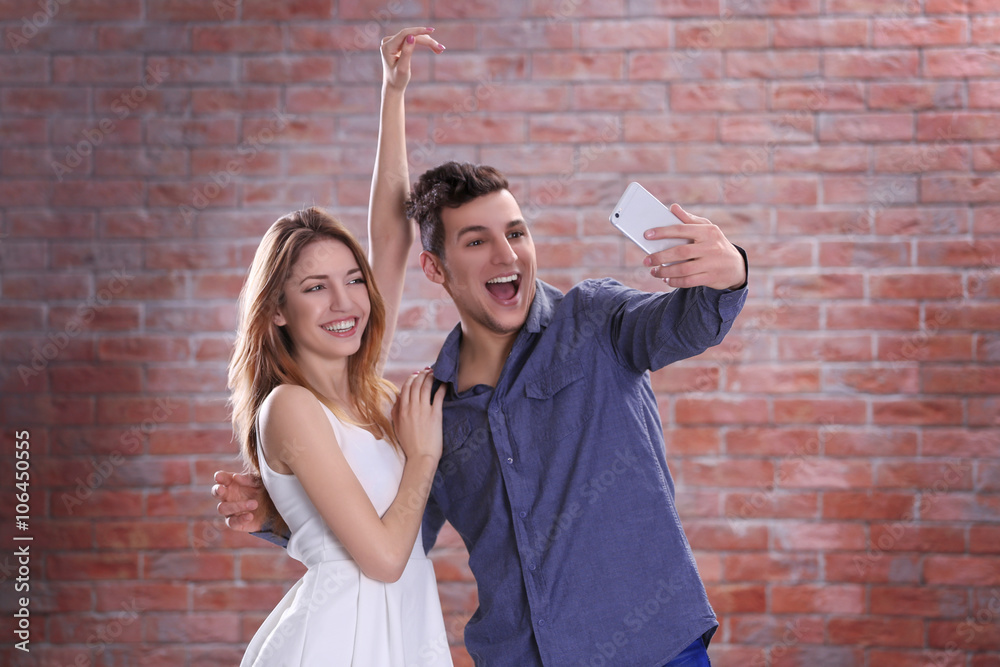 Young attractive couple taking selfie with mobile phone on brick wall background
