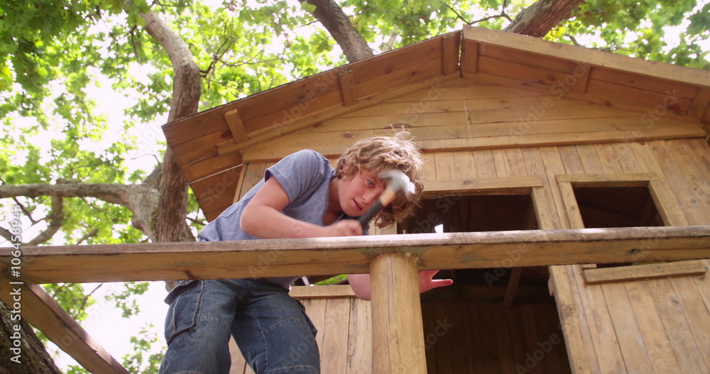 Boy repairing his wooden treehouse with a hammer and nail