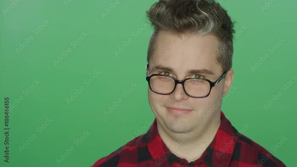 Young man with glasses starts laughing, on a green screen studio background