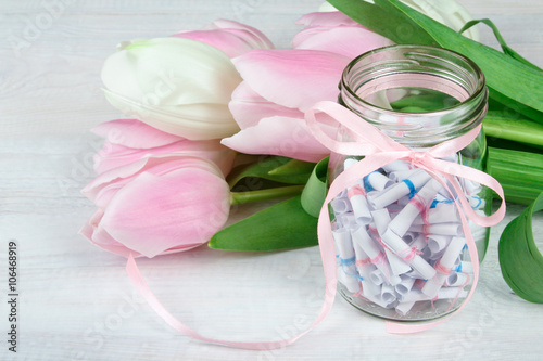 beautiful pink and white tulips laid on wooden background with a jar in which lie small twisted note