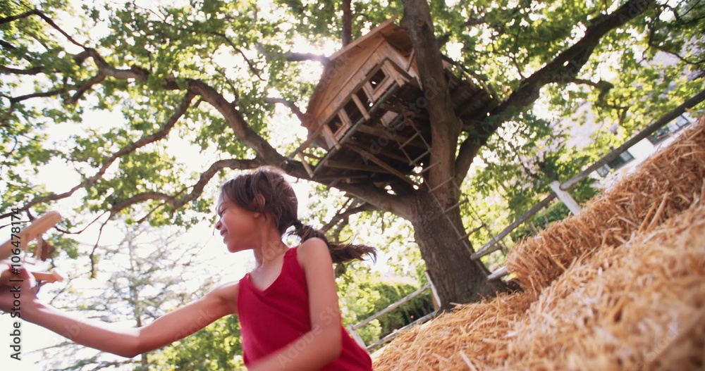 Little girl playing under a tree with toy wooden plane