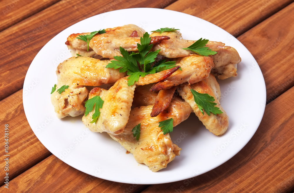 Plate with baked chicken wings and parsley on a wooden background Plate with baked chicken wings and parsley on a wooden background