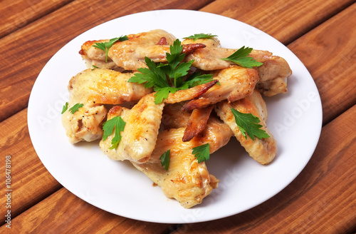 Plate with baked chicken wings and parsley on a wooden background