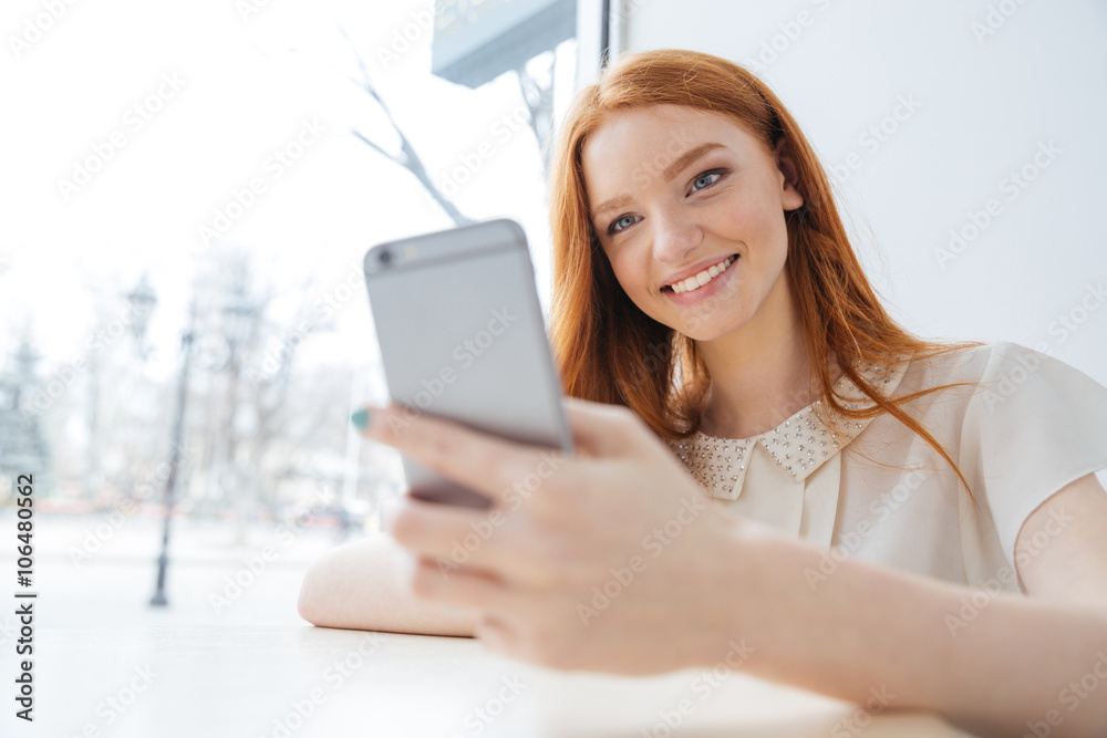 Cheerful woman with long red hair using smartphone in cafe Cheerful woman with long red hair using smartphone in cafe