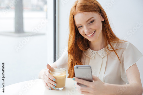 Smiling woman sitting in cafe and using cell phone