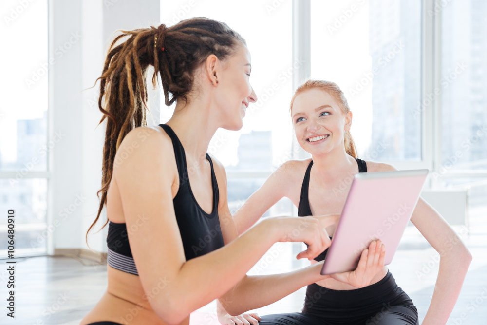 Two cheerful sportswomen using tablet together
