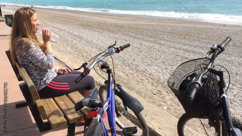 Young girl sitting on seafron and drinking water. On the background of the sea, near the bike.  photo