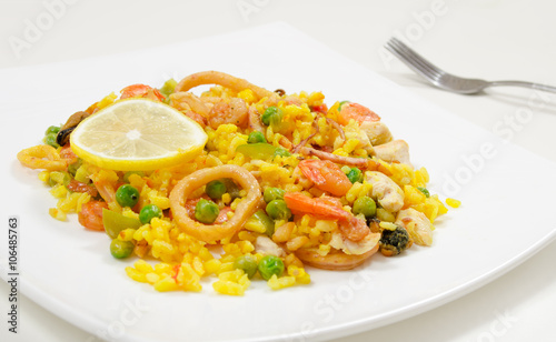 Paella with chicken and seafood on a white plate, close-up, side view
