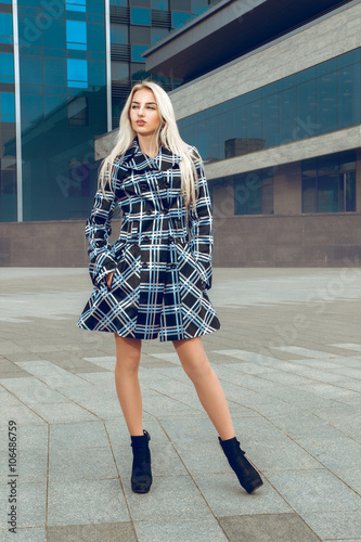 Serious young blonde fashion model in the coat posing outdoors a