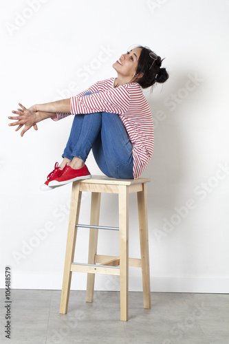 Quadro su tela student vacation smile - happy gorgeous ethnic girl relaxing on a stool enjoying free time, white background studio
