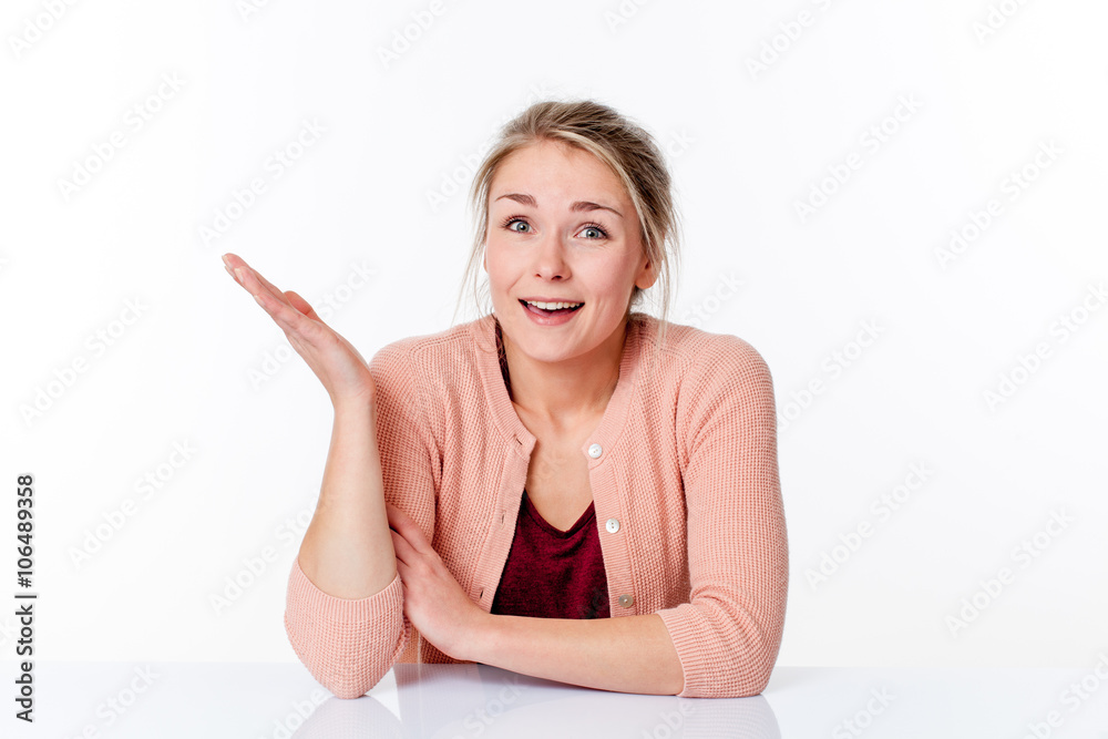 serene smile - cheerful young blond woman sitting in a sparse office smiling and showing something up, white background studio. serene smile - cheerful young blond woman sitting in a sparse office smiling and showing something up, white background studio.