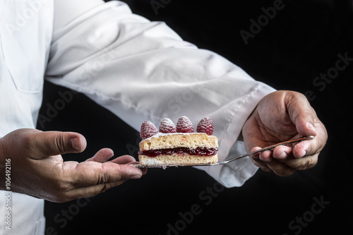 Chef man hands with a cake over black background, close up detai