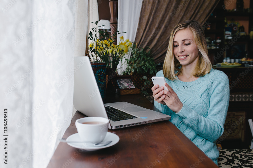 Fototapeta premium Portrait of successful young woman with laptop in street cafe. Young woman using laptop in a cafe. Side portrait of a cool young modern woman using mobile phone at cafe