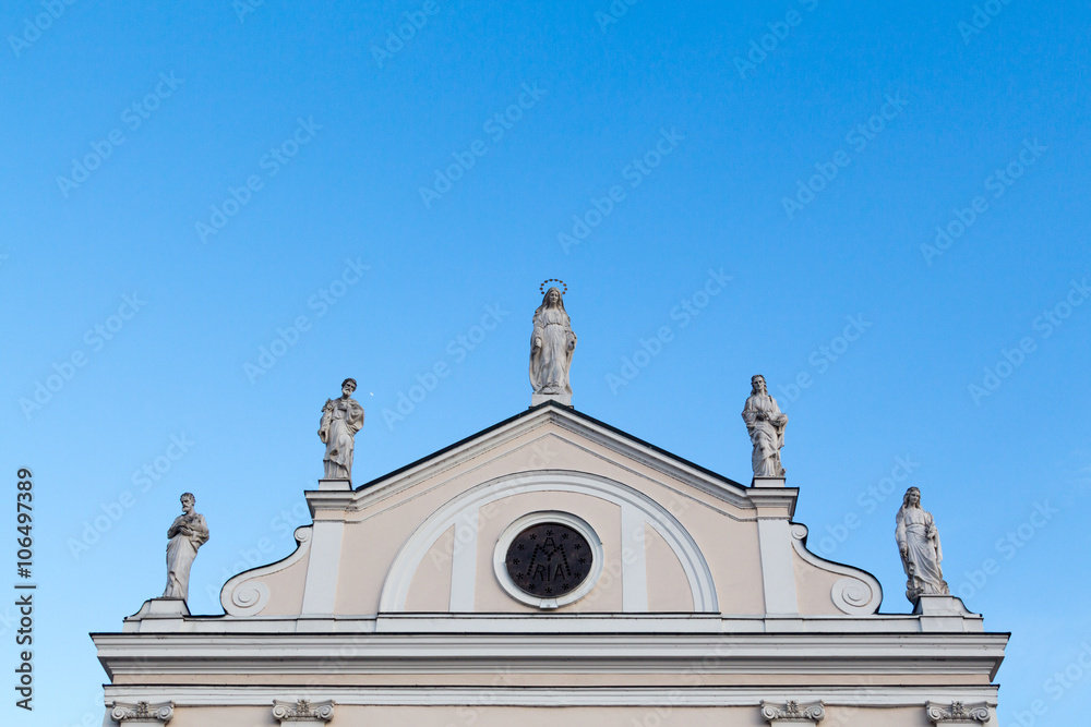Kamnik, Slovenia - January 25, 2016. Religious statues on the top of the facade of the Church of the Immaculate Conception on the background of blue sky.