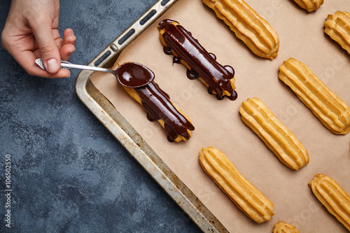 Obraz na plátně Eclairs or profiterole with chocolate and whipped cream preparing on baking sheet