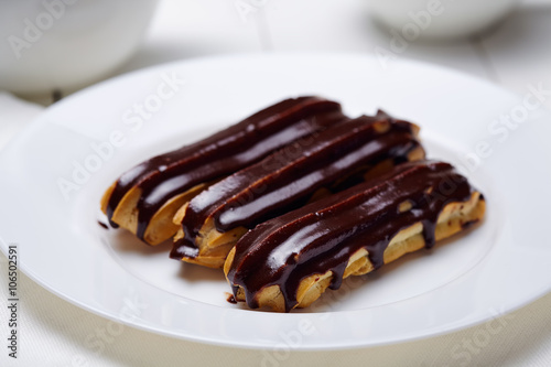 Eclairs or profiteroles with chocolate icing and whipped cream on white dish background.