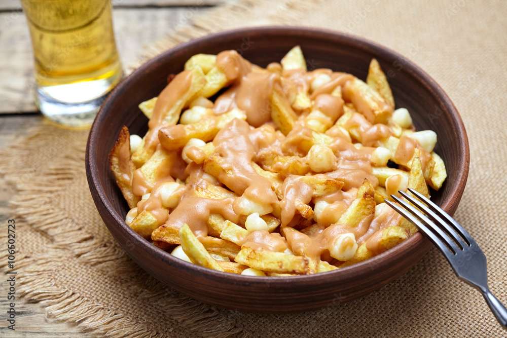 Poutine Quebec traditional meal with fries, curd cheese and gravy on vintage wooden table background. Rustic style Poutine Quebec traditional meal with fries, curd cheese and gravy on vintage wooden table background. Rustic style