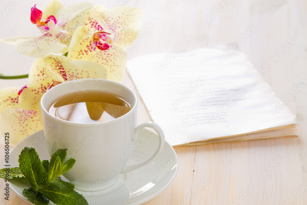 A cup of green tea with yellow blotchy orchid flowers and fresh mint