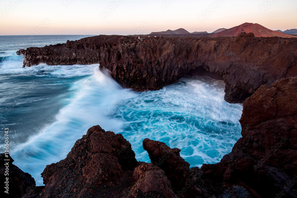 Los Hervideros rocky coast with wavy ocean and volcanos on the background on the sunset on Lanzarote island in Spain. Long exposure effect with blurred water