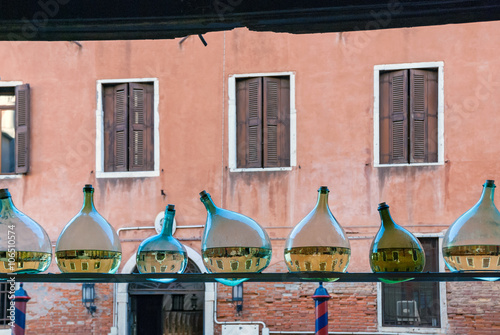 Row of glass bottles half filled with water showing reflection of Venice water canal, building from the opposite side of street with closed windows, blinded with window shutters. Venice, Italy.