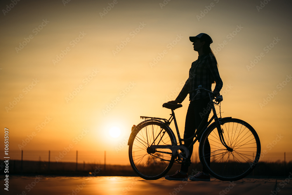 beautiful hipster girl with a bicycle on the road during sunset