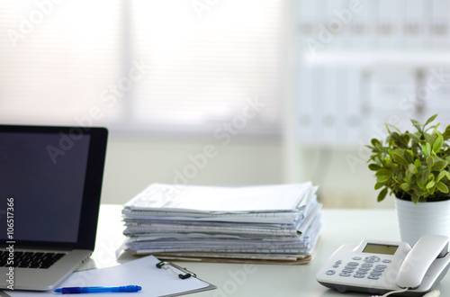 Laptop with stack of folders on table on white background © lenetsnikolai