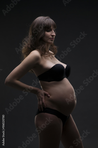 Young beauty and sexy caucasian pregnant woman in black lingerie on gray studio background © staras