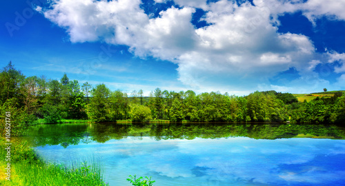  Lake and green trees on sky background.