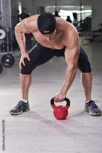 Handsome powerful athletic man performing kettle bell exercise. Strong bodybuilder with perfect shoulders, biceps and triceps.