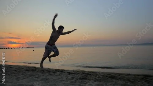 Slow motion steadicam shot of a young man performing flips and somersaults on the beach at sunset. Acrobatics on the sand photo