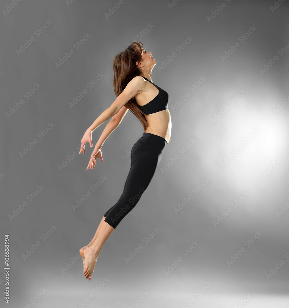 Fototapeta premium Young sporty woman jumping on grey background