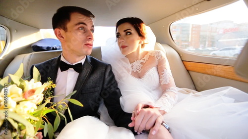 Bride and groom in love sitting on a car, holding hands and talking with each others.