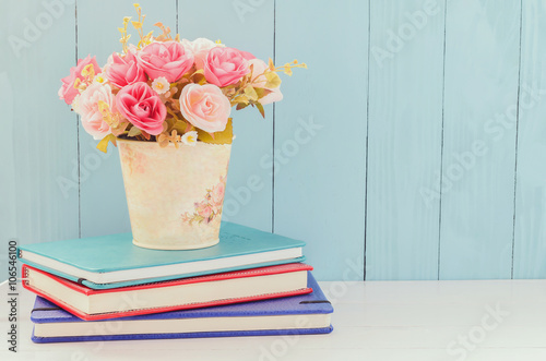 Artificial Rose in flower pot with pile of notebooks