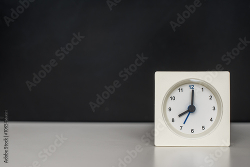 white clock on a white table against the background of black board.