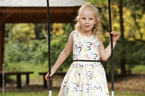 Attractive 5 years old blond girl wearing light dress at outdoor park