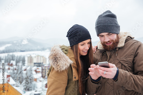 Happy couple using smartphone together in winter photo