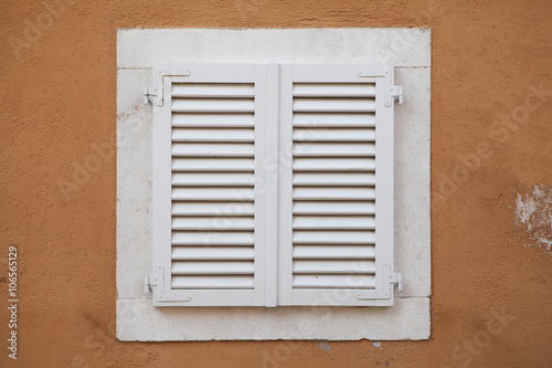 White window with shutters in yellow wall