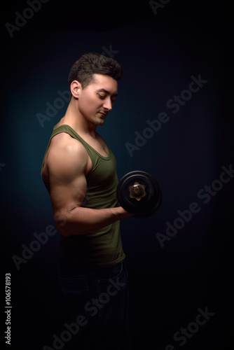 Muscle man training with dumbbell on dark background
