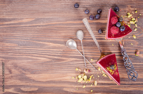 Piece of delicious raspberry cake with fresh raspberries, blueberry, currants and pistachios on shovel, wooden background. Free space for your text. photo