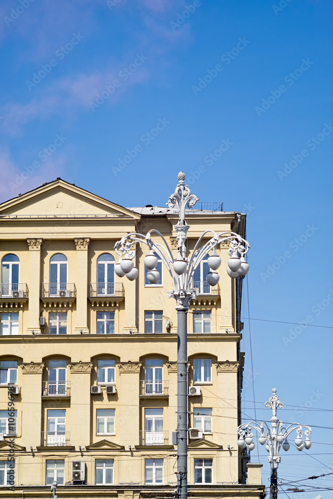 Old building face with stucco molding and street lamps before against blue sky background. Moscow, Russia. 
