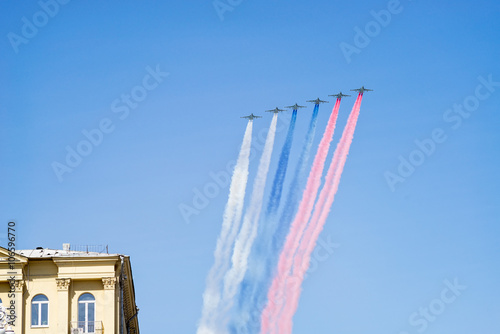 Su-25BM Frogfoot jet aircrafts with color smokes of tricolor fly on blue sky over building photo