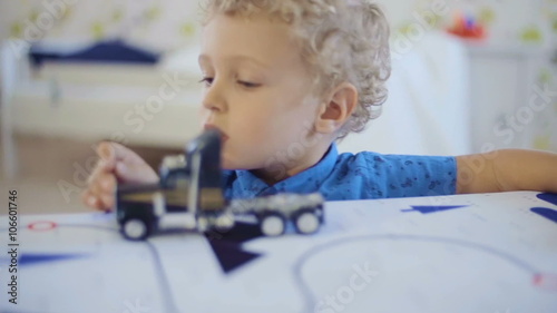 Little curly-headed boy playing with toy truck