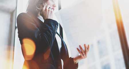 Photo business woman wearing white shirt, talking smartphone and holding documents in hands. Open space loft office. Panoramic windows background. Wide mockup, film effect, bokeh