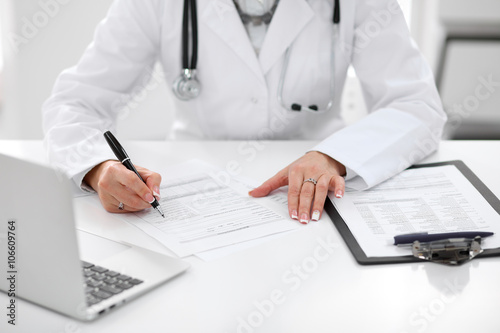 Close-up of a female doctor filling out application form , sitting at the table in the hospital