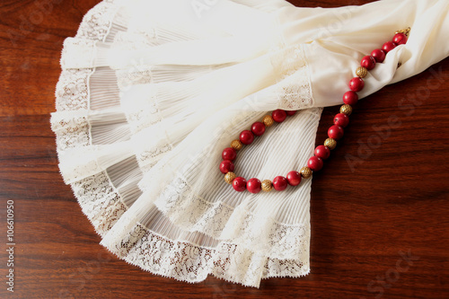 Fotografie A white lace petticoat with a red coral necklace with golden spheres on a brown, wooden table